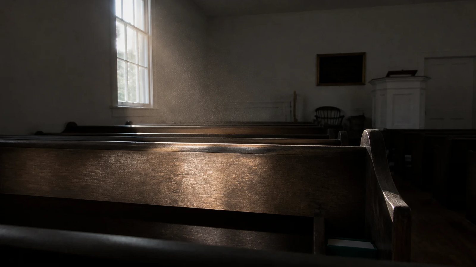 Morning light falling across the back of an old wooden pew in an empty New England church